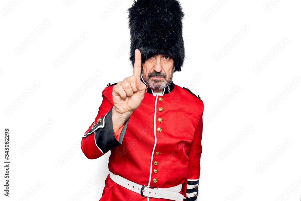Middle age handsome wales guard man wearing traditional uniform over white background Pointing with finger up and angry expression, showing no gesture Middle age handsome wales guard man wearing traditional uniform over white background Pointing with finger up and angry expression, showing no gesture