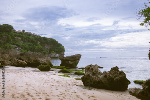 Beautiful deserted beach on the island of Bali at sunset. Rocks and nature. Plants and houses on the coast. Tropical paradise. Stones and white sand on the ocean