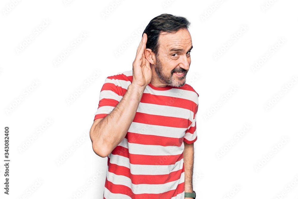Middle age handsome man wearing striped t-shirt standing over isolated white background smiling with hand over ear listening and hearing to rumor or gossip. Deafness concept. Middle age handsome man wearing striped t-shirt standing over isolated white background smiling with hand over ear listening and hearing to rumor or gossip. Deafness concept.
