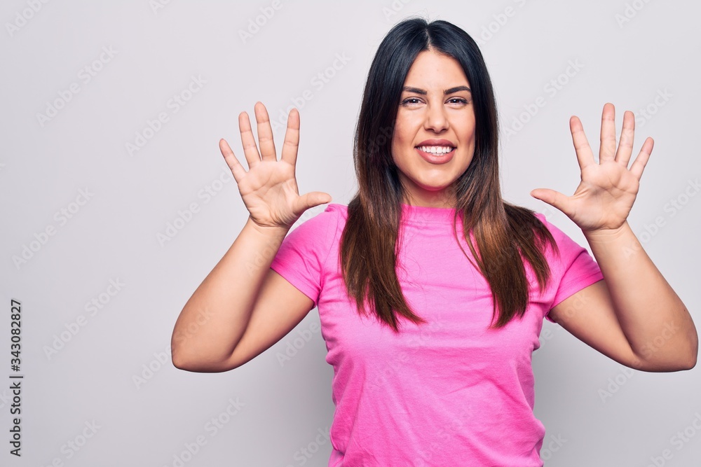 Young beautiful brunette woman wearing casual pink t-shirt standing over white background showing and pointing up with fingers number ten while smiling confident and happy. Young beautiful brunette woman wearing casual pink t-shirt standing over white background showing and pointing up with fingers number ten while smiling confident and happy.