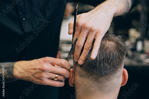 Young hipster man with hearty beard cutting his hair in a barbershop. Professional hairdressing work. Lifestyle