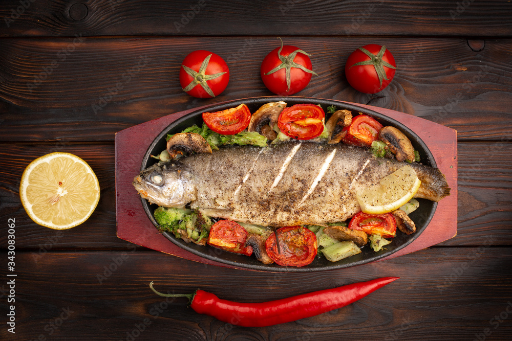 baked trout with vegetables on an oval plate on a dark wooden background