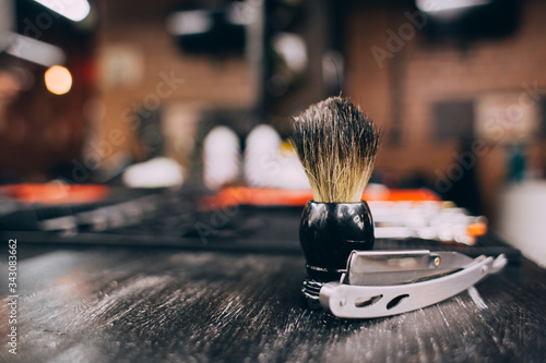 straight razor, brush for shaving beard along with bowl, blurred background of hair salon for men, barber shop