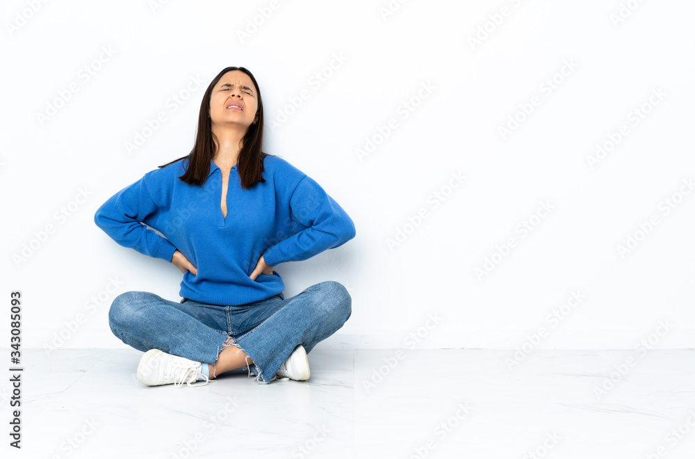 Young mixed race woman sitting on the floor isolated on white background suffering from backache for having made an effort Young mixed race woman sitting on the floor isolated on white background suffering from backache for having made an effort