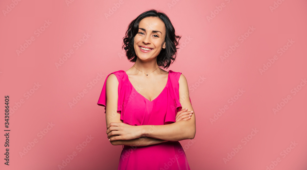 True lady. Close-up photo of a charming healthy woman in a fuchsia dress, who is looking in the camera and smiling, while standing with her arms folded. True lady. Close-up photo of a charming healthy woman in a fuchsia dress, who is looking in the camera and smiling, while standing with her arms folded.