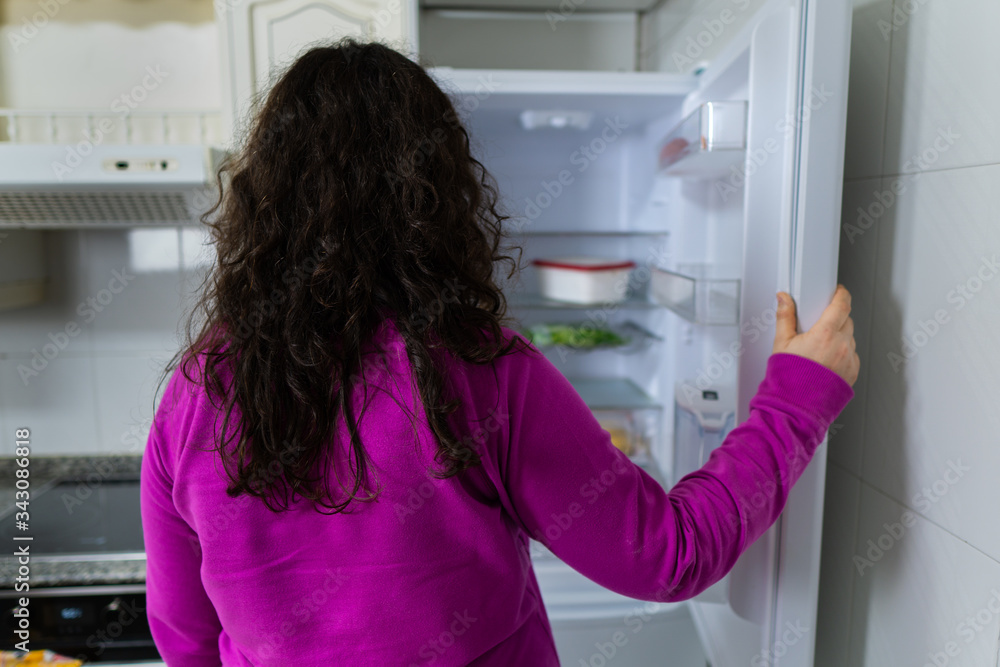 Señora blanca de dad media abre la nevera vacía sin comida porque no tiene dinero debido a la crisis económica. Tiene un jersey violeta y la nevera es blanca. Señora blanca de dad media abre la nevera vacía sin comida porque no tiene dinero debido a la crisis económica. Tiene un jersey violeta y la nevera es blanca.