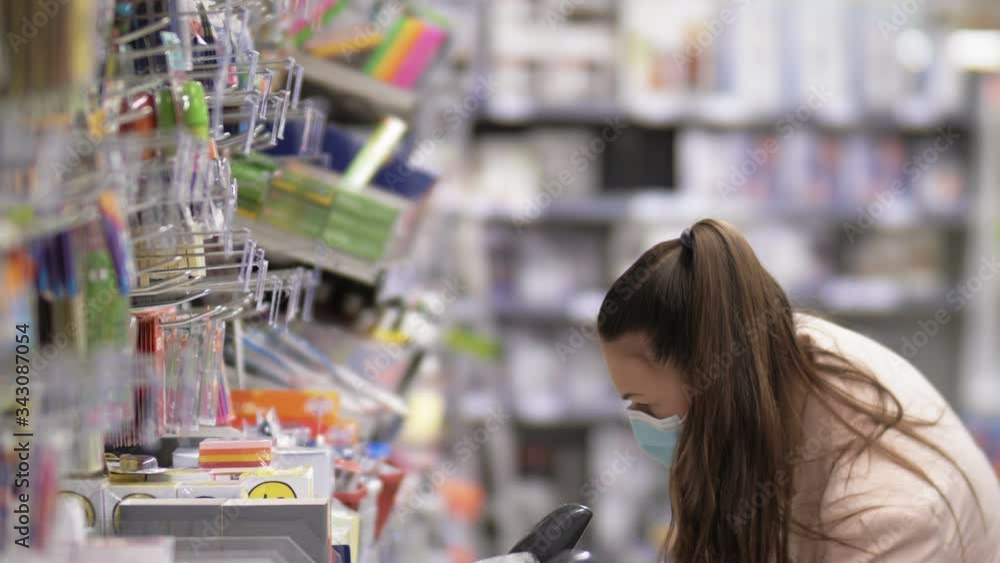 Shopper woman wearing a protective mask and gloves examines stationery in a supermarket. Covid-19. Shopper woman wearing a protective mask and gloves examines stationery in a supermarket. Covid-19.