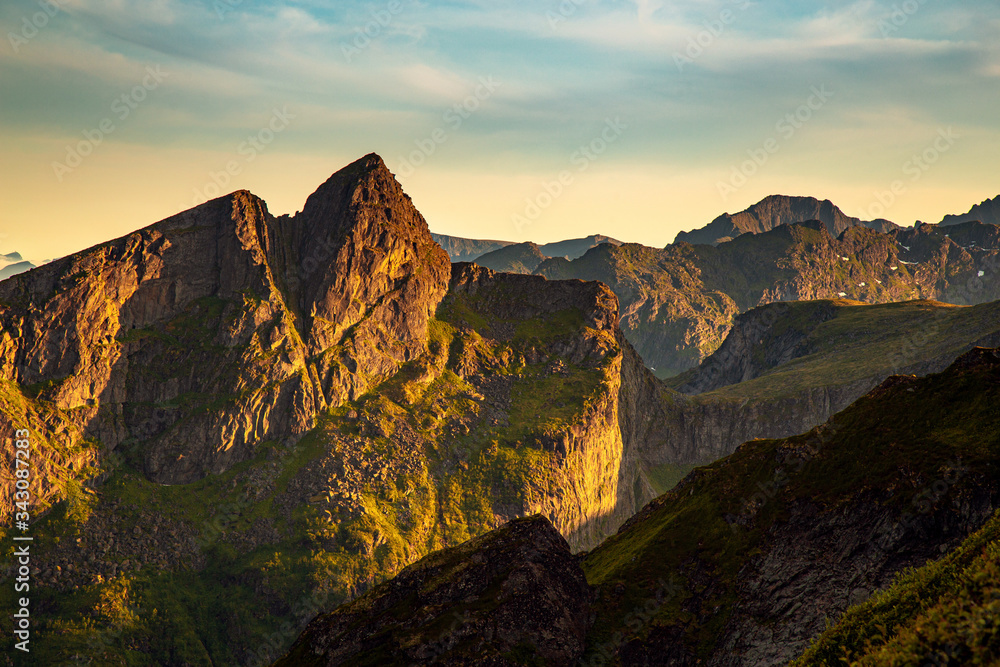 Sunset across a rugged mountain range in the Lofoten region of Norway during summer. Nobody visible in the photo.