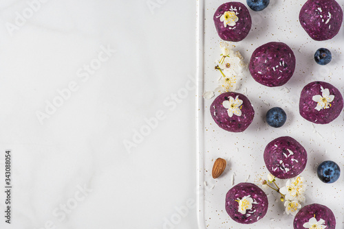 Raw vegan energy balls or bites made of blueberry, acai, nuts and dates served with flowers. top view with copy space