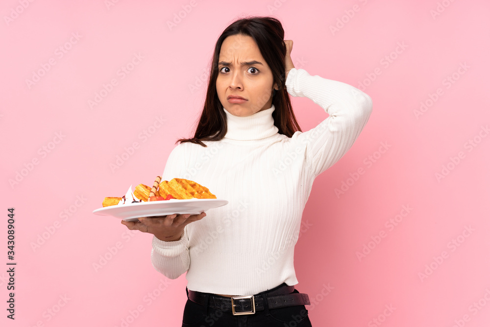Young brunette woman holding waffles over isolated pink background having doubts Young brunette woman holding waffles over isolated pink background having doubts