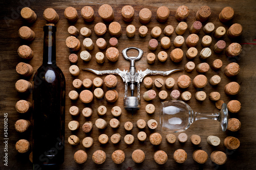 Wine corks of different sizes, a corkscrew, a bottle of wine and a glass shot on an old wooden surface. Background for liquor.