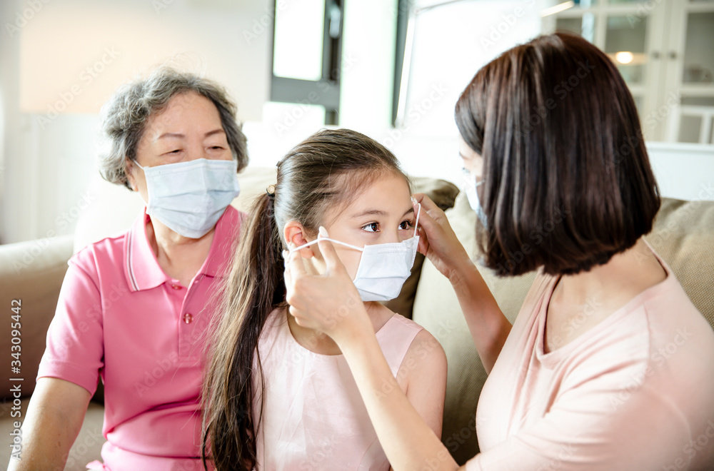 mother and grandmother help daughter wearing face mask to prevent  air pollution and COVID-19 coronavirus