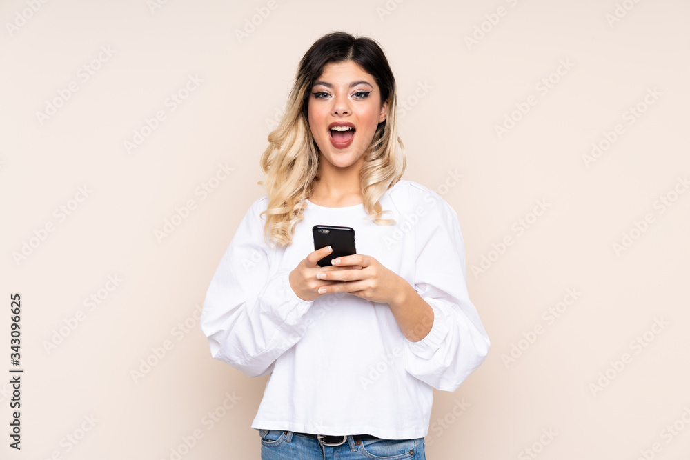 Teenager girl isolated on beige background surprised and sending a message Teenager girl isolated on beige background surprised and sending a message