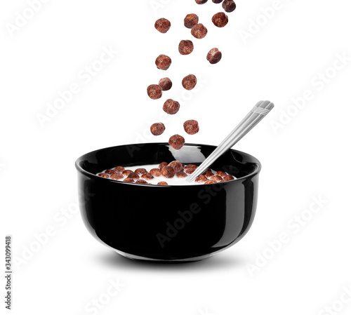 Falling chocolate cereal balls in milk in a black bowl isolated on a white background