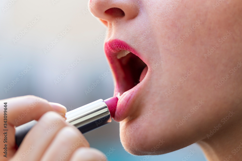 Woman applying red lipstick on lip