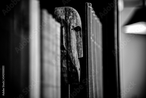 Canvastavla scultura di testa di legno africana in mezzo a un a libreria densa di libri
