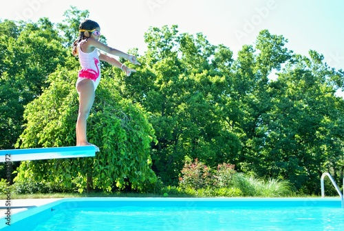 фотографія little girl with goggles on getting ready to jump into a swimming pool from a di