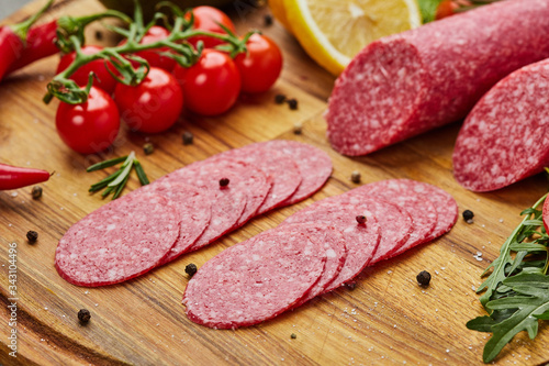 Traditional thinly sliced salami on a wooden cuttingboard with spices, lettuce, avocado and tomatoes. Cold meat plate