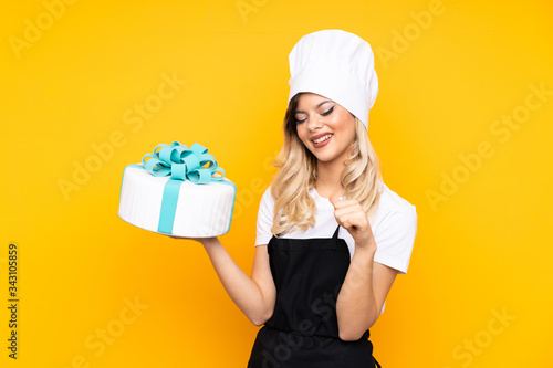 Teenager girl pastry holding a big cake isolated on yellow background proud and self-satisfied