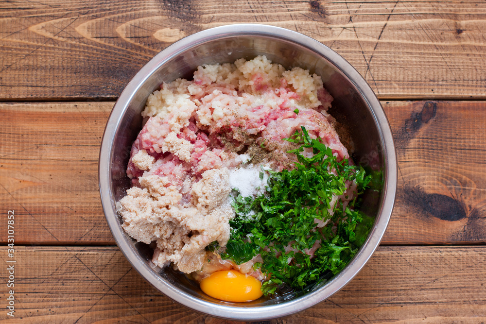 Step-by-step cooking of steamed turkey cutlets, step 3 - mixing the minced meat with herbs, egg and spices, top view, selective focus Step-by-step cooking of steamed turkey cutlets, step 3 - mixing the minced meat with herbs, egg and spices, top view, selective focus