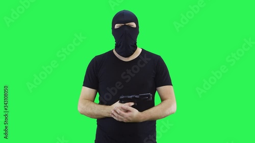 A man in a balaclava says to the camera holding a gun in his hands then makes a headshot.Temple shot.Green screen background.