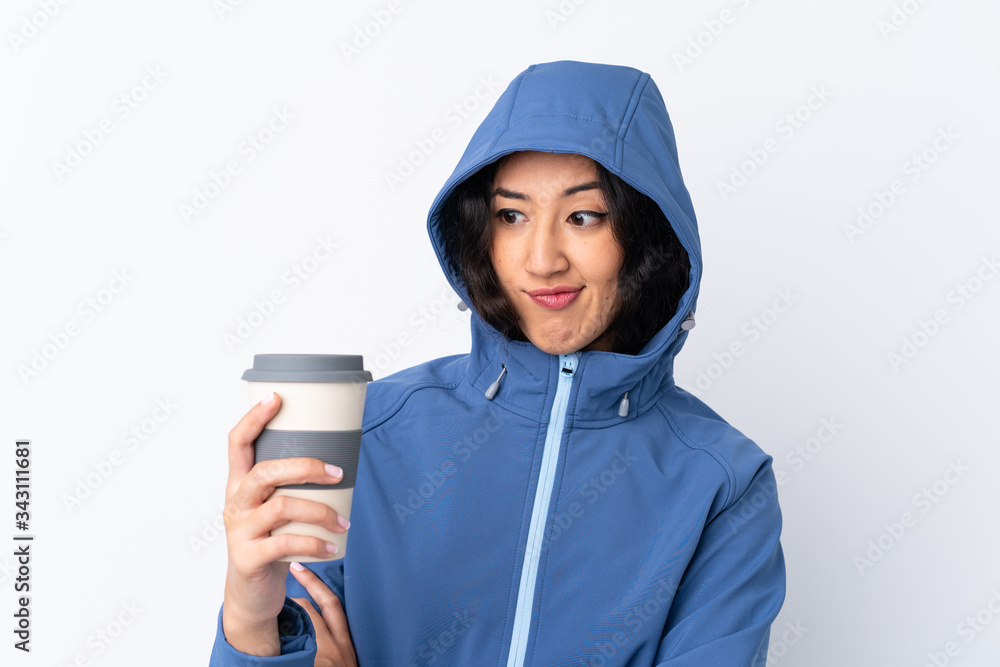 Mixed race woman wearing winter clothes with the hood on and holding a hot takeaway coffee over isolated white background with sad expression