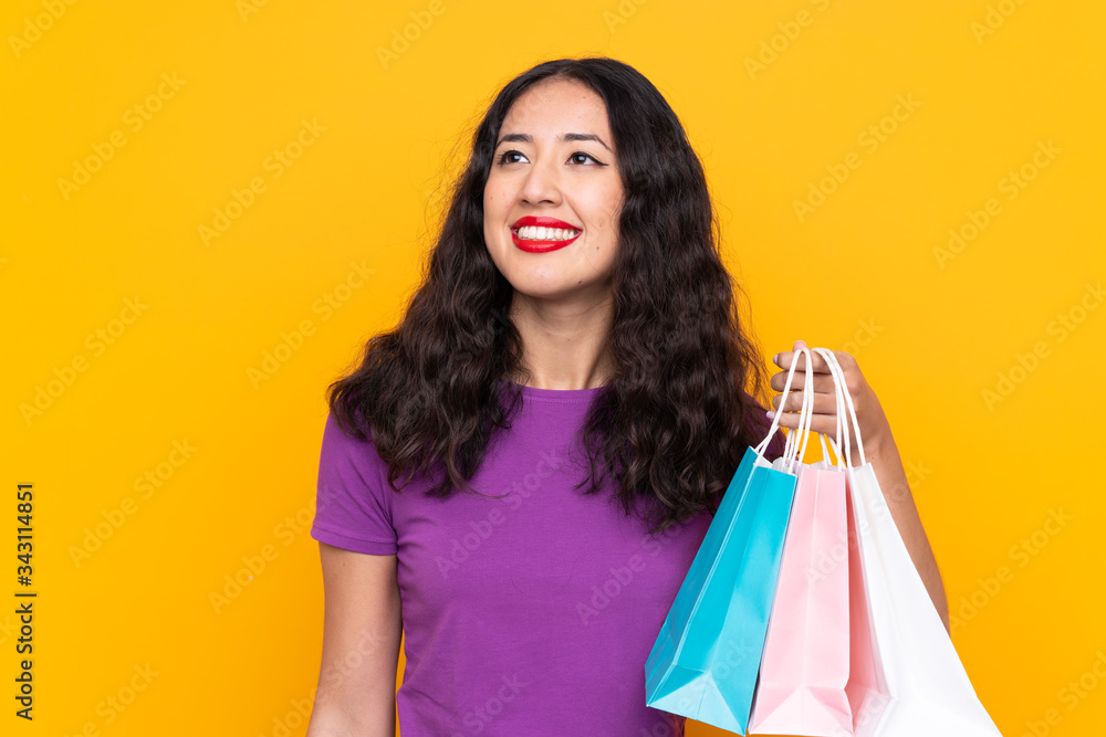 Spanish Chinese woman with shopping bag over isolated background looking up while smiling
