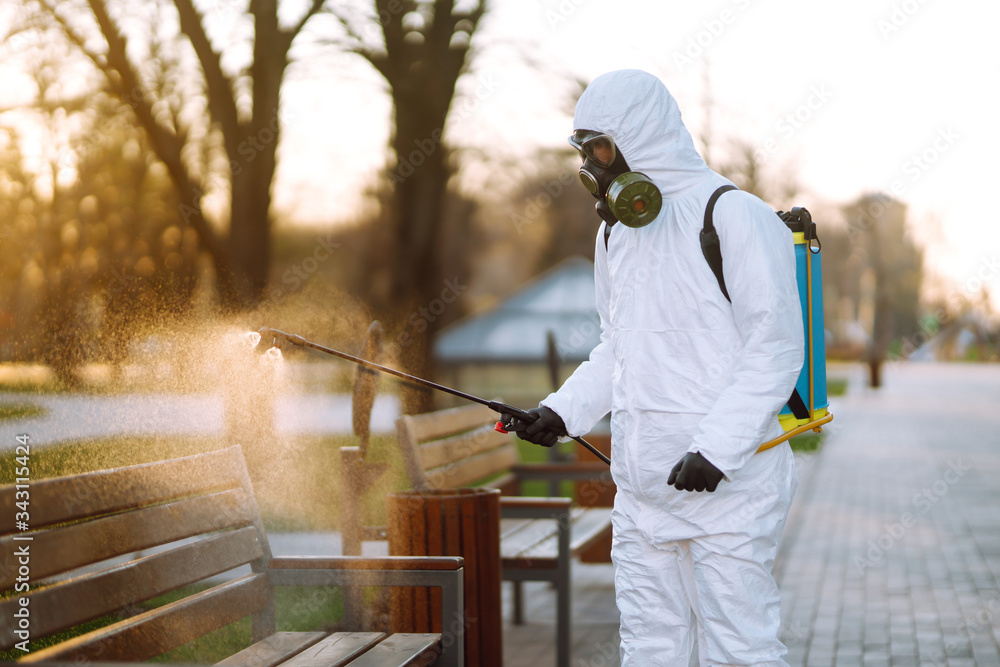 Man in protective suit disinfecting bench in the public park in quarantine city. Infection prevention and control of epidemic. Covid -19. Man in protective suit disinfecting bench in the public park in quarantine city. Infection prevention and control of epidemic. Covid -19.