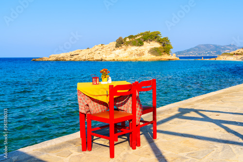 Taverna table with red chairs on coastal promenade with sea in background in Kokkari village, Samos island, Greece