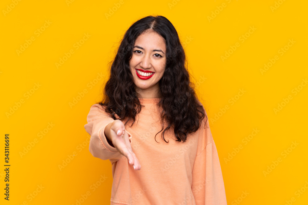 Spanish Chinese woman over isolated yellow background shaking hands for closing a good deal Spanish Chinese woman over isolated yellow background shaking hands for closing a good deal