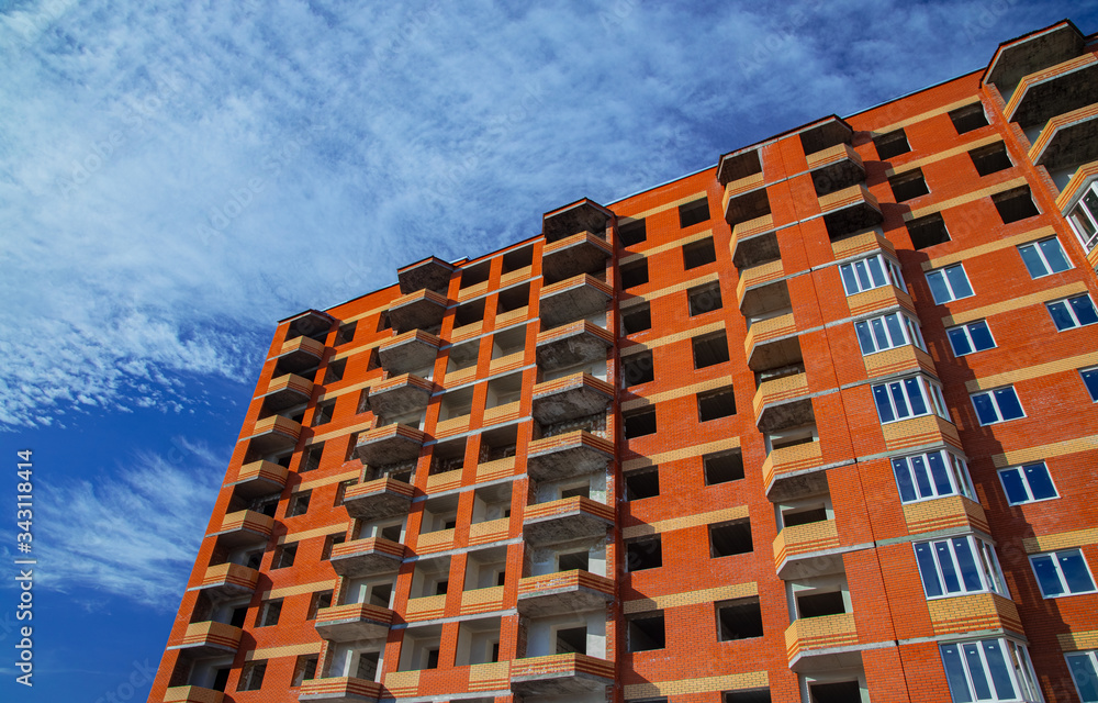 unfinished living building brick exterior facade architecture construction shape object foreshortening from below in sun lighting on blue sky background