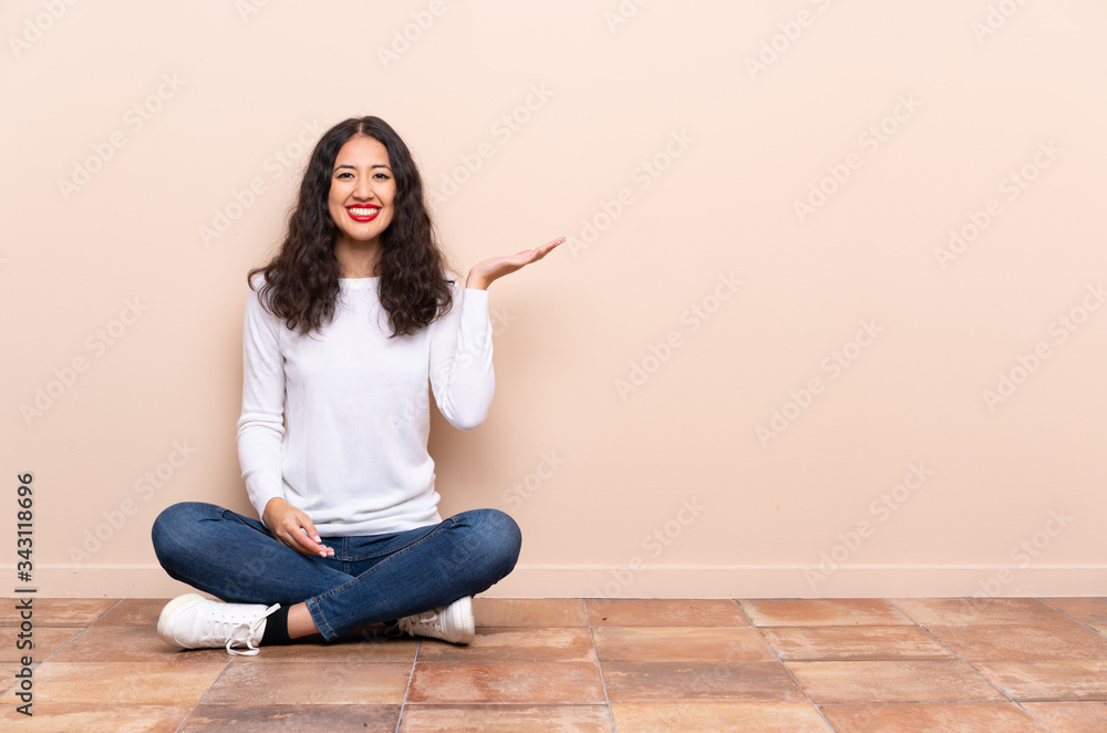 Young woman sitting on the floor holding copyspace imaginary on the palm to insert an ad