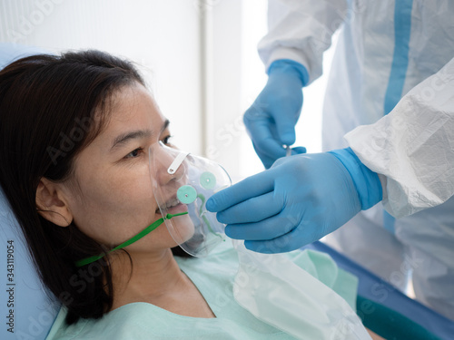 Asian doctor wear PPE suit treat and use oxygen mask or emergency inhalation mask with coronavirus infected patient in negative pressure quarantine room. Coronavirus, medical and covid19 concept.