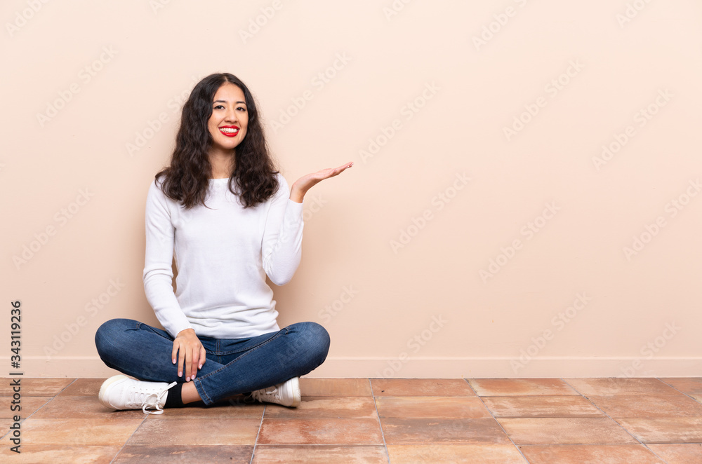 Young woman sitting on the floor presenting an idea while looking smiling towards
