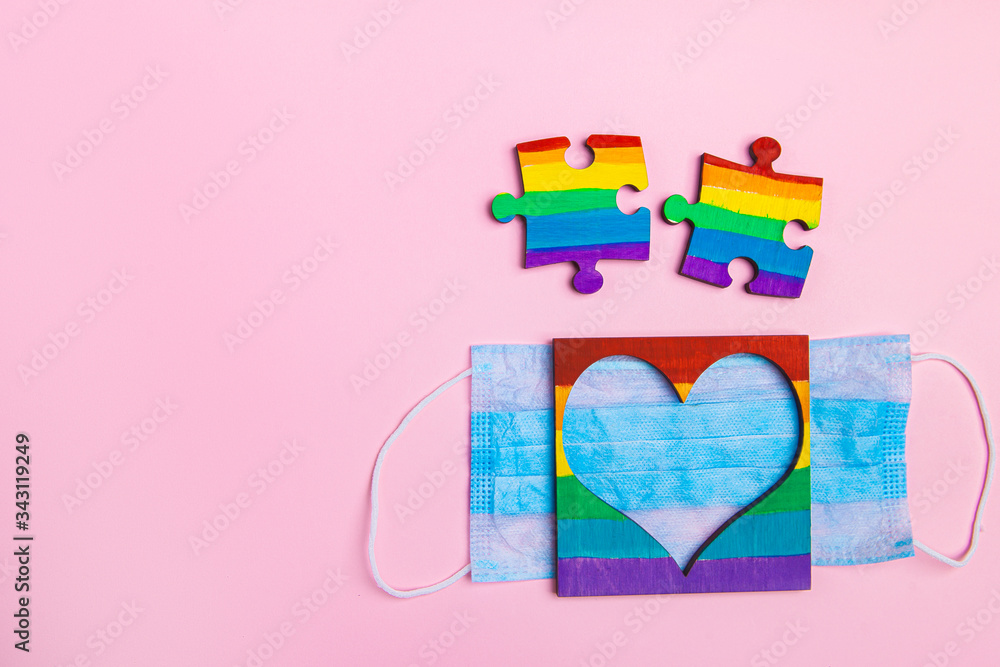 LGBT symbol puzzles and heart frame painted by a rainbow on a medical mask. Coronavirus quarantine, online festival and pride day 2020. copy-space. space for text on a pink background