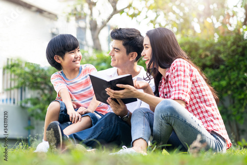 Family happy activity. Asian mother and father holding book sitting in garden backyard at home. Little cute boy kid reading the book with happiness. Son smiling to parent enjoy spending time together.