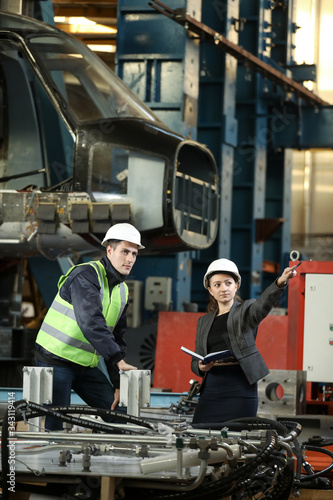 Portrait of a female factory manager in a white hard hat and business suit and factory engineer in work clothes. Controlling the work process at the airplane manufacturer. 