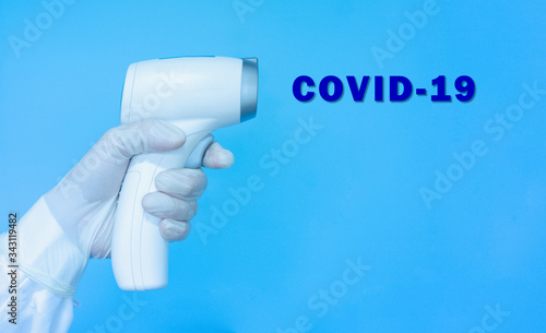 Woman doctor wearing gloves, holding medical infrared forehead thermometer or thermometer gun for checking and screening body temperature with text Covid-19. Coronavirus, covid-19 and medical concept.