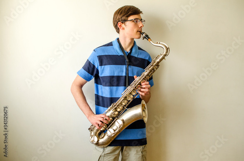 Obraz na plátně Young saxophonist plays tenor saxophone in a striped blue shirt on a white backg