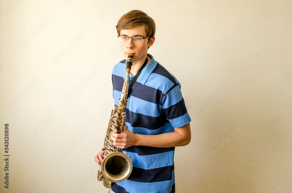 Naklejka premium Young saxophonist plays tenor saxophone in a striped blue shirt on a white background 