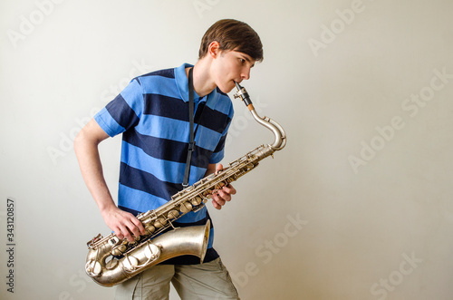 Photos Young saxophonist plays tenor saxophone in a striped blue shirt on a white backg