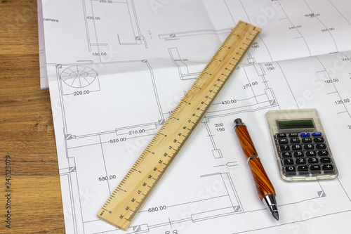 desk with building construction plan resting on top with ruler, pencil and calculator © christian cantarelli