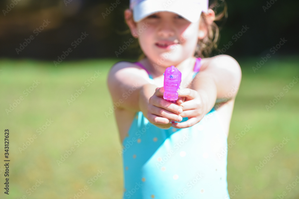 Young girl shooting a water pistol outside on a hot day in the garden water pistol in the foreground Young girl shooting a water pistol outside on a hot day in the garden water pistol in the foreground