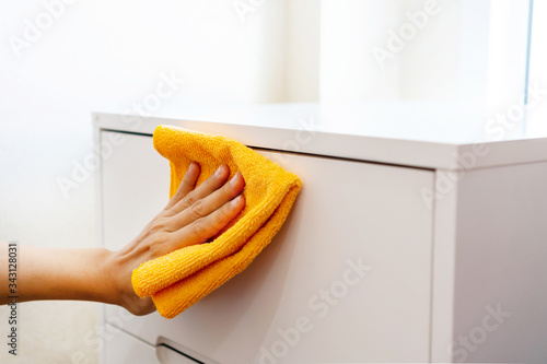 Woman hand cleaning white cabinet with orange color microfiber cloth in bedroom at home. Concept of disinfecting surfaces from bacteria or viruses. Close up photo