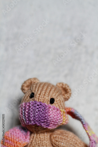 kleiner gestrickter Teddy mit Schal als Mundschutz, Gesichtsmaske, als Schutz vor Corona, vor einer weissen Wand. © Barbara-Maria Damrau