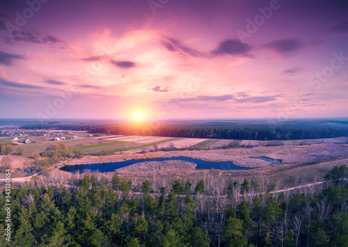 Spring rural landscape in the evening with a beautiful burning sky. Aerial view. Panoramic view of pine forest  fields  and river during blazing sunset