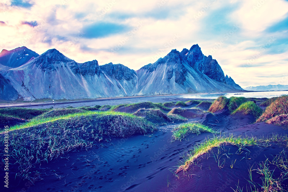 Scenic landscape with most beautiful mountains Vestrahorn on the Stokksnes peninsula and cozy lagoon with green grass on the sand dunes at sunset in Iceland. Exotic countries. Amazing places.