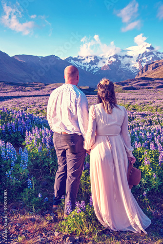 Obraz na płótnie Beautiful landscape with oung couple in lupine flowers on a background of mountains in Iceland. Magical places. Exotic countries. w salonie