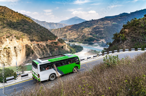 A white-green bus moves along the serpentine mountain road against the background of a river valley among the mountains.