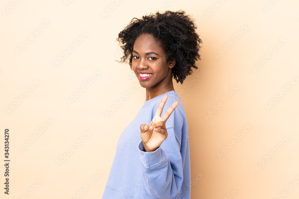 Young African American woman isolated on beige background smiling and showing victory sign Young African American woman isolated on beige background smiling and showing victory sign